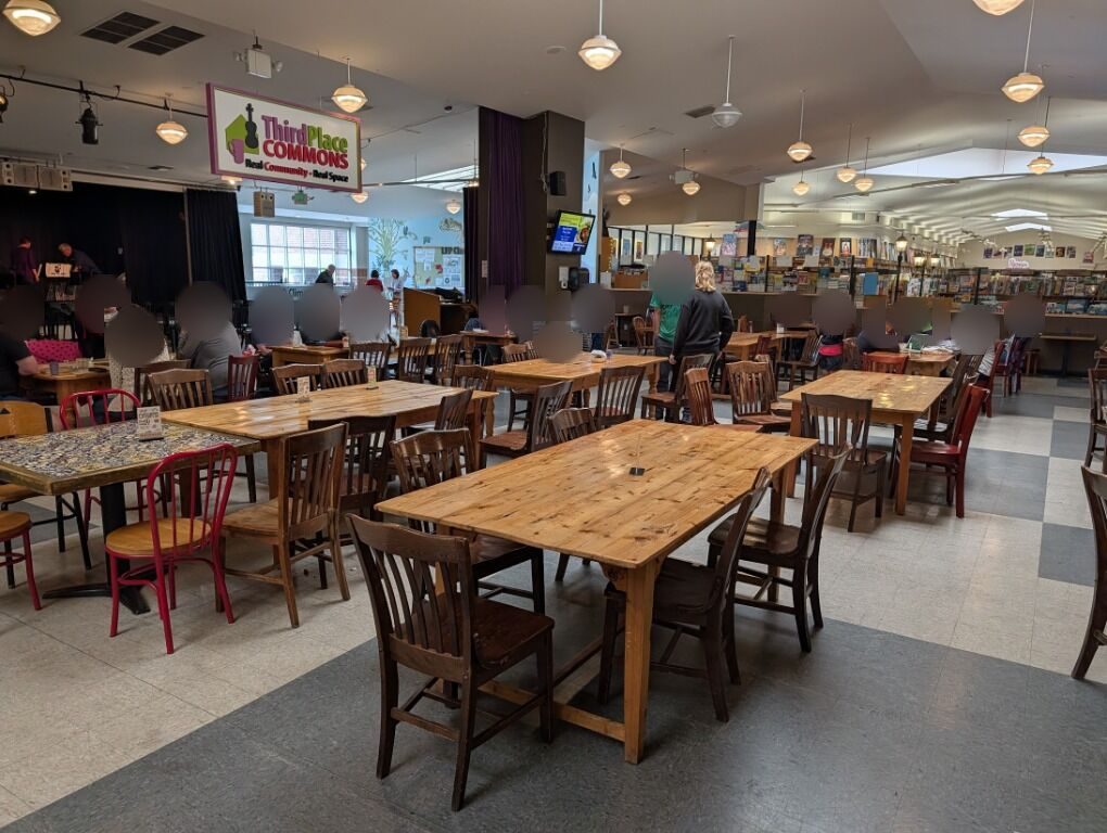 The open table seating area at Third Place Commons: long wooden tables and chairs on a tiled floor, with the stage and the Third Place Commons sign in the background.